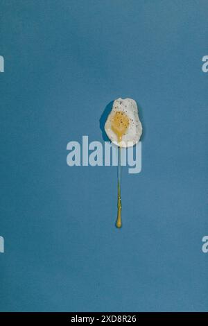 Fried egg yolk dripping on blue background Stock Photo