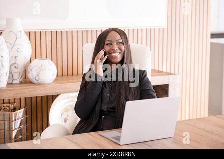 Laughing woman on phone while working on laptop Stock Photo