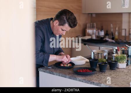 Chef plating food in a modern kitchen with herbs and utensils Stock Photo