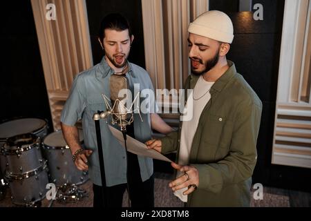 Two men stand side by side in a recording studio, collaborating creatively on music for their band rehearsal. Stock Photo