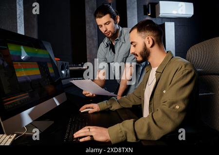 Two men are collaborating on a computer in a recording studio, working on music for their band rehearsal. Stock Photo