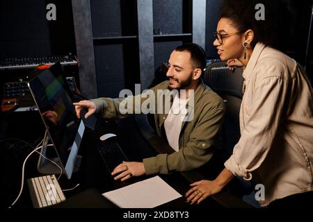 A man and woman collaborate on a computer in a recording studio during a music band rehearsal. Stock Photo