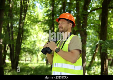 Forester with binoculars examining plants in forest Stock Photo