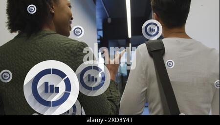 Image of multiple bar graph icons floating against two diverse women discussing at office Stock Photo