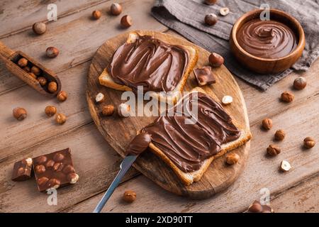 Board of bread with chocolate paste and hazelnuts on wooden background. Popular desser food. Top view. Stock Photo