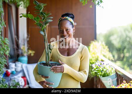 Smiling woman holding potted plants on the balcony at home Stock Photo