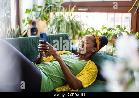 Woman using smartphone while relaxing on sofa at home Stock Photo
