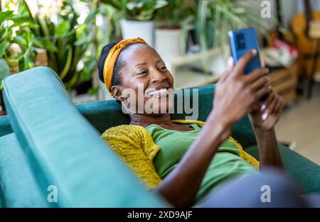 Woman using smartphone while relaxing on sofa at home Stock Photo