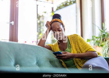 Woman using smartphone while relaxing on sofa at home Stock Photo