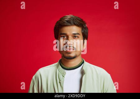 Portrait of young middle eastern man in casual attire looking at camera calmly against red studio background. Stock Photo
