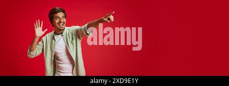 Banner. Excited young Indian man pointing at distance against red studio background with negative space to insert text. . Stock Photo