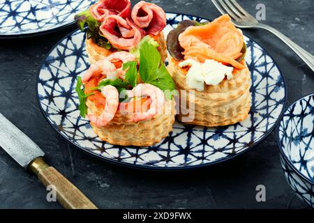 Puff pastry tartlets with fish, shrimp and bacon on a plate on the table. Stock Photo
