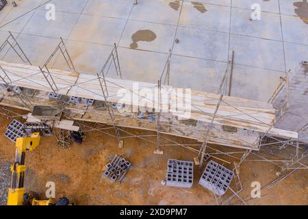 An experienced bricklayer stands on scaffolding to construct working concrete wall from concrete blocks Stock Photo