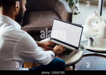Over shoulder view of a young business man using computer laptop in front of an blank white computer screen in his home living room. Photo ready for m Stock Photo
