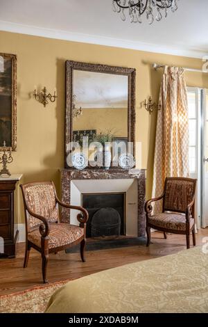 Pair of upholstered armchairs at fireside in yellow bedroom in renovated stone-built hotel particulier dating from 1770 in Saulieu, Burgundy, France. Stock Photo