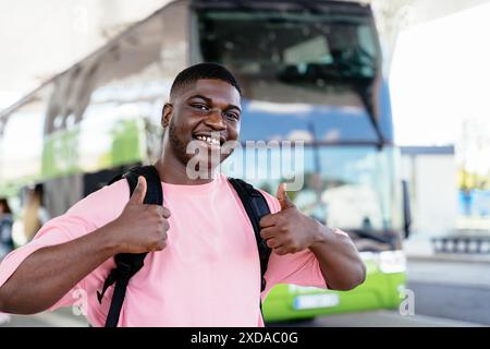 A man wearing a pink shirt and backpack is smiling and giving thumbs up Stock Photo