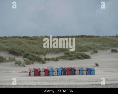 Row of colourful beach chairs along a sandy beach with high dunes in the background under a cloudy sky, Juist, North Sea, Germany Stock Photo