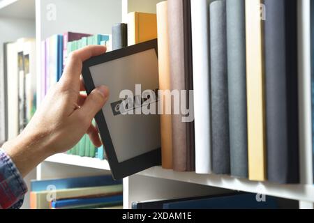 Detail of hand taking an ebook from a white shelf full of books. Front view. Stock Photo