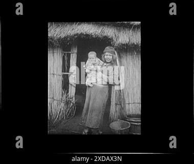 Ainu woman holding a child standing outside a hut. Genthe photograph collection. Stock Photo