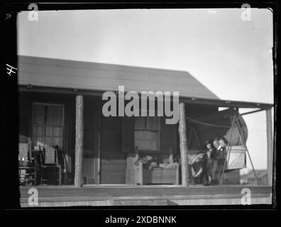 Arnold Genthe and two women friends seated on a swing on the porch of his bungalow in Long Beach, New York. Genthe photograph collection. Stock Photo