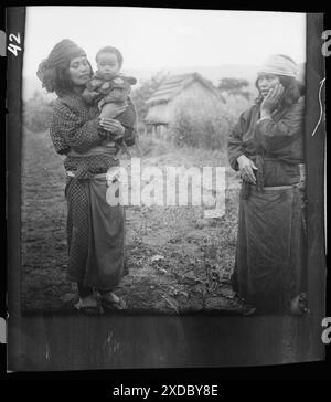 Two Ainu woman, one holding a child, standing outside. Genthe photograph collection. Stock Photo