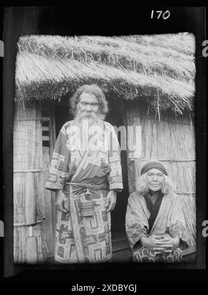 Ainu man and seated woman at the entrance of a hut. Genthe photograph collection. Stock Photo