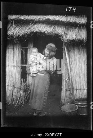 Ainu woman holding a child standing outside a hut. Genthe photograph collection. Stock Photo