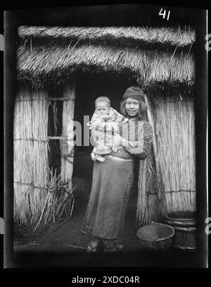 Ainu woman holding a child standing outside a hut. Genthe photograph collection. Stock Photo