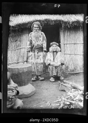 Ainu man and seated woman at the entrance of a hut. Genthe photograph collection. Stock Photo