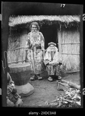 Ainu man and seated woman at the entrance of a hut. Genthe photograph collection. Stock Photo