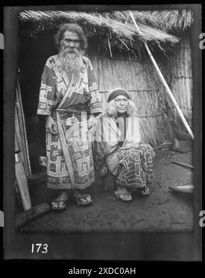 Ainu man and seated woman at the entrance of a hut. Genthe photograph collection. Stock Photo