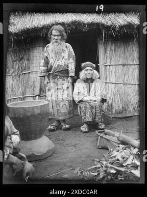 Ainu man and seated woman at the entrance of a hut. Genthe photograph collection. Stock Photo