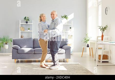 Smiling cheerful senior family couple wife and husband dancing in living room at home. Stock Photo