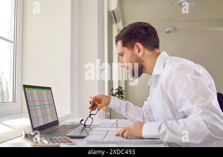 Businessman sitting at table in office looking at report on computer screen Stock Photo