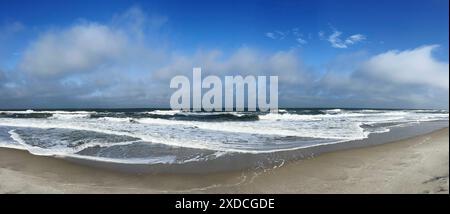 The image captures a panoramic view of the Atlantic Ocean coastline on a Summer day. Whitecaps crest the blue waves as they crash against the sandy sh Stock Photo