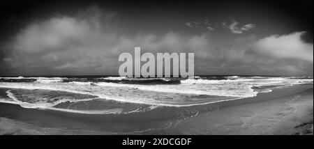 Black and white image capturing a panoramic view of the Atlantic Ocean coastline on a Summer day. Whitecaps crest the blue waves as they crash against Stock Photo