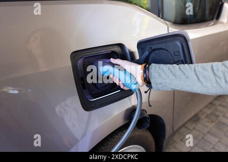 Charging electric car, female hand holding plug and connecting it to the vehicle Stock Photo