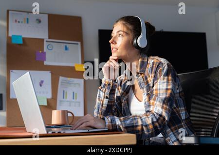 Wearing headphones and using laptop, young woman is working at home Stock Photo