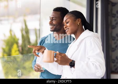 Standing on balcony, young couple drinking morning coffee and looking at view Stock Photo