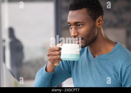 Man in blue sweater drinking from mug, looking thoughtful at home Stock Photo