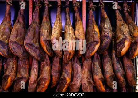 Selling jamon at the market. Ham in the form of pork butts hangs on the counter, awaiting customers. National product of Spain. Stock Photo