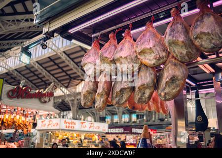 Valencia, Spain 1.03.2024: Selling jamon at the market. Ham in the form of pork butts hangs on the counter, awaiting customers. National product of Sp Stock Photo