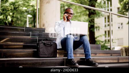 Young African American businessman using his laptop outside an urban office building, networking with diverse traders for cryptocurrency advancement. Stock Photo