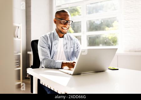 African American businessman laughing at his modern office while analyzing financial markets and utilizing PC technology. Successful executive manager Stock Photo