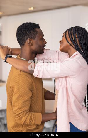 Young Black couple embracing, smiling at each other in cozy home setting Stock Photo