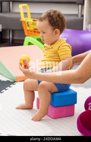 Female physical therapist working with infant on motor skills and coordination in rehab clinic. Male child patient with body hypotonia in physical the Stock Photo