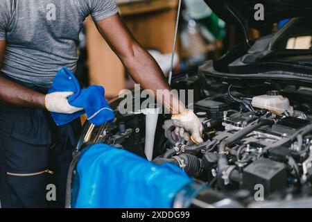 Garage Mechanic African Black male professional working car auto service checking engine oil at front hood. Stock Photo
