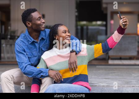 Young African American couple sitting together, taking selfie with smartphone Stock Photo