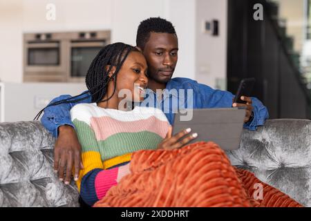 Young couple relaxing on couch, using devices for social media or chatting at home Stock Photo