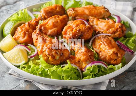 Tom yum chicken wings deep fried served with onions and lime close up in a plate on the table. Horizontal Stock Photo